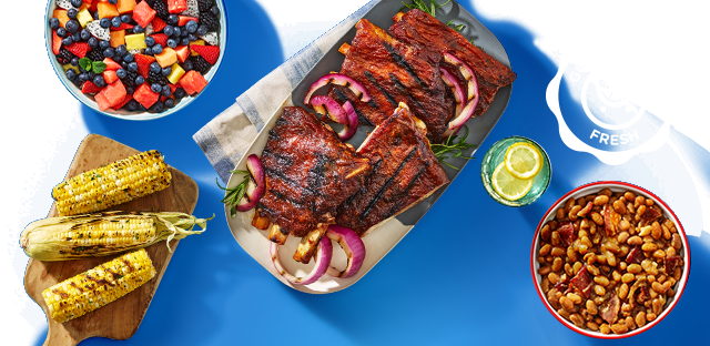 Grilled ribs, corn, beans, and mixed fruit display.