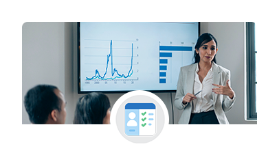 A businesswoman, standing in front of a screen with two  data charts, talking with an audience.