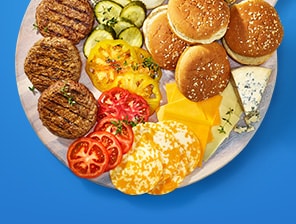Platter of buns, lettuce, grilled hamburger patties and sliced tomatoes, onions and cheese. 