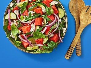 Bowl of fresh salad with leafy arugula and mint, watermelon, cucumber, feta and red onion.