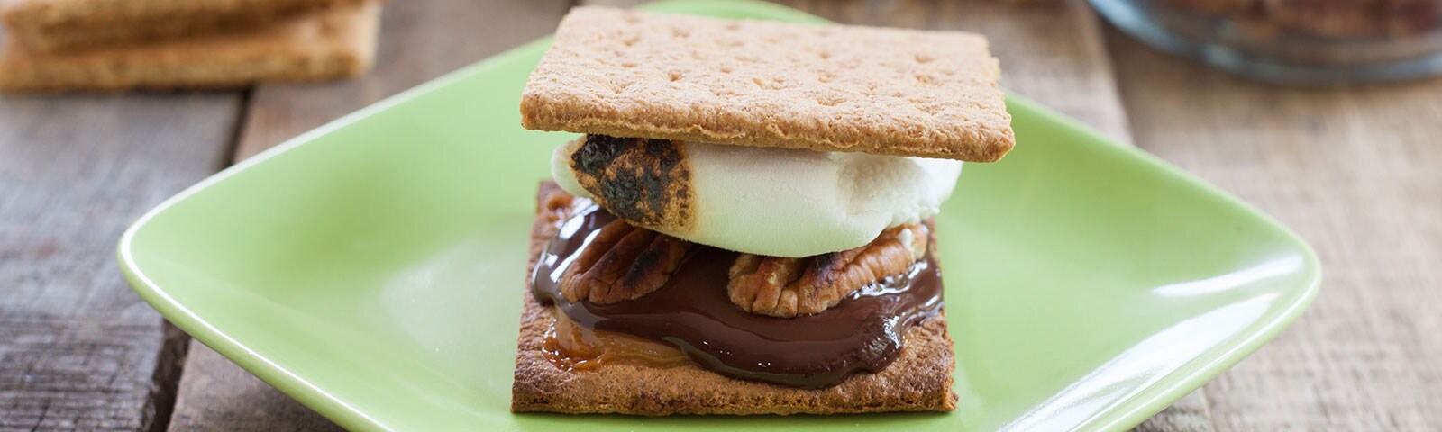 A smore with pecans and chocolate on a green plate A smore with pecans and chocolate on a green plate