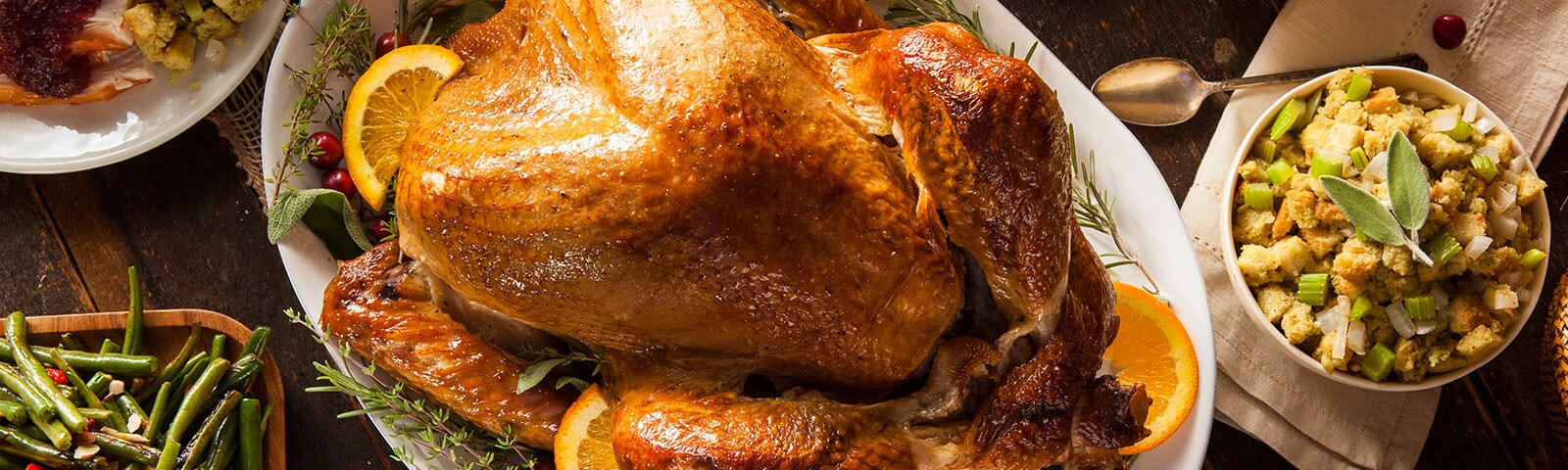 A rustic wooden table covered in various thanksgiving side dishes with a large turkey on a serving plate in the center A rustic wooden table covered in various thanksgiving side dishes with a large turkey on a serving plate in the center
