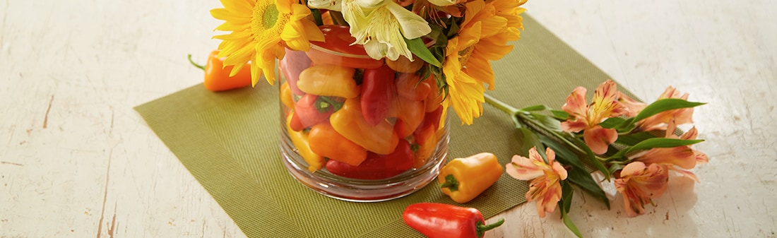 A vase full of multicolored mini peppers with sunflowers coming out of the top A vase full of multicolored mini peppers with sunflowers coming out of the top