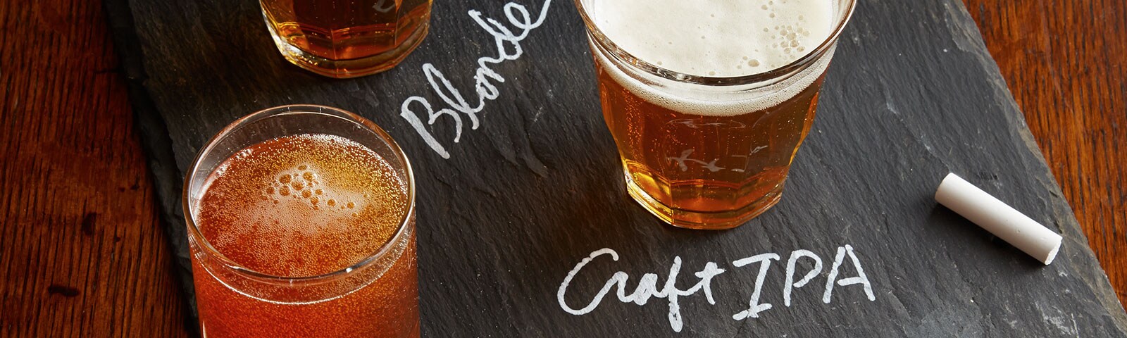 Craft beer flight with a row of glasses on a chalkboard and the words "Blonde" and "Craft IPA" written out in chalk