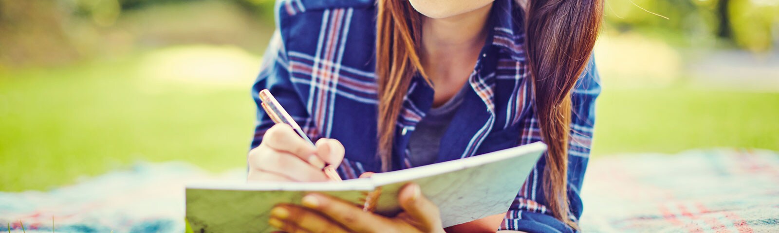 Woman laying on a picnic blanket outside in the grass writing in her journal Woman laying on a picnic blanket outside in the grass writing in her journal