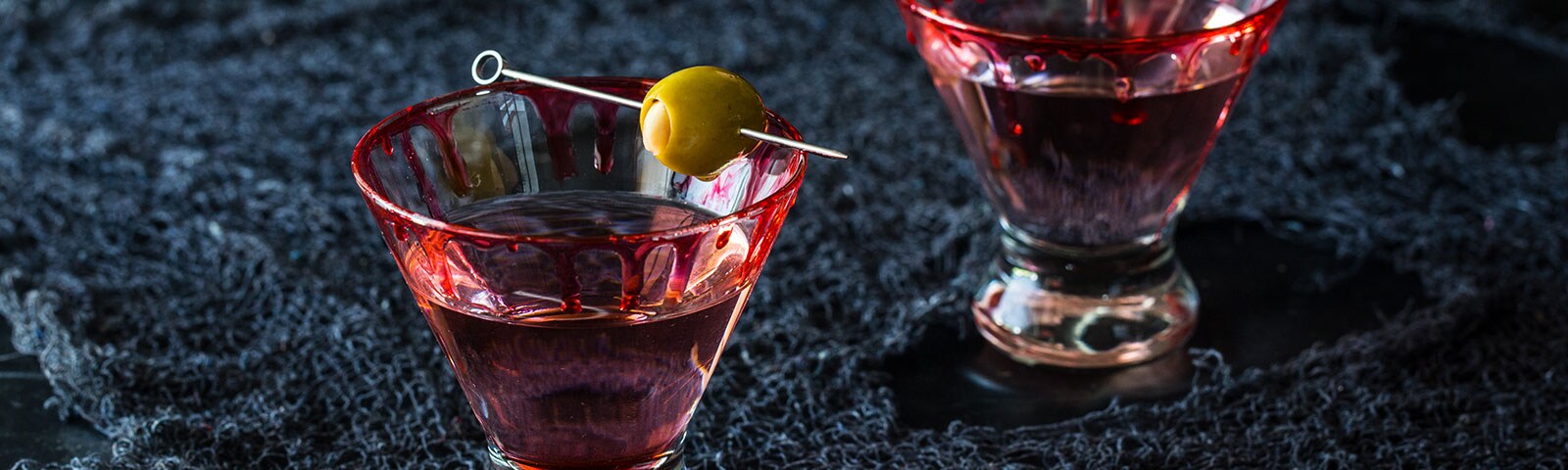 Two cocktail glasses with red liquid dripping down their sides sit on a dark blue cloth Two cocktail glasses with red liquid dripping down their sides sit on a dark blue cloth