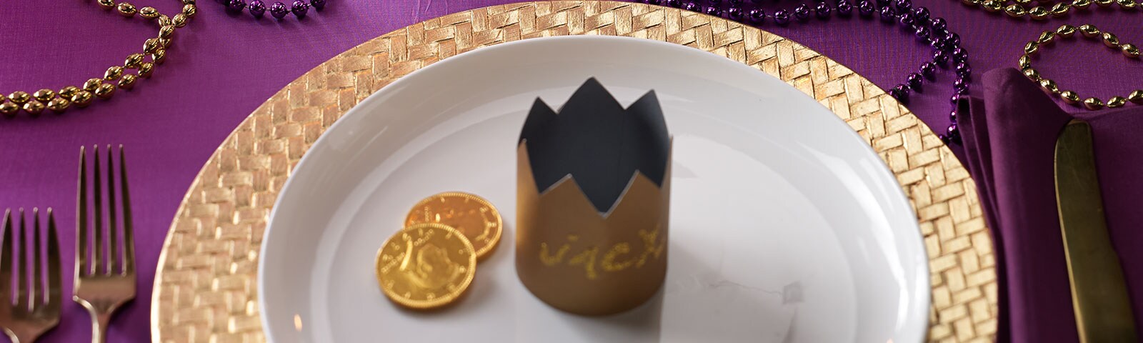 Mardi Gras-themed table decor featuring gold chargers and placemats on a purple tablecloth surrounded by gold and purple beads