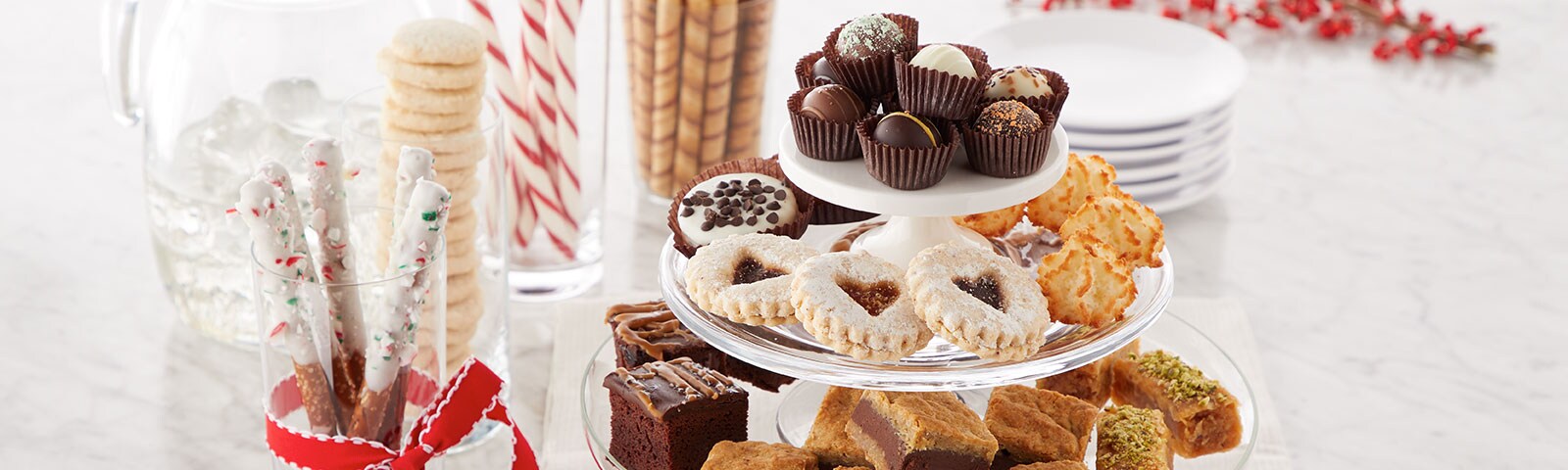 A cake platter filled with pastries on a table next to chocolate-dipped pretzel sticks and other treats in jars or vases A cake platter filled with pastries on a table next to chocolate-dipped pretzel sticks and other treats in jars or vases