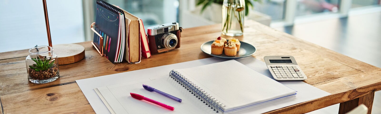 Pen and paper on wooden desk with cupcakes and plant Pen and paper on wooden desk with cupcakes and plant