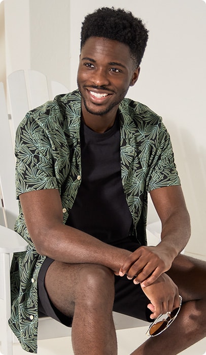 A relaxed man with a leafy patterned over shirt with a black tank top underneath.